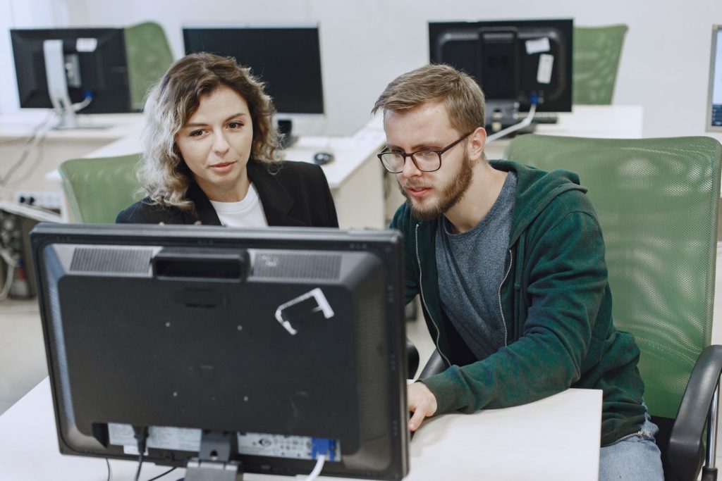 Jeune formatrice accompagnant un collaborateur sur son poste informatique pendant une formation logiciel en salle