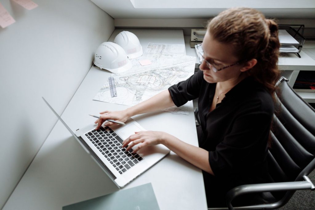 Gestionnaire d’une entreprise du bâtiment travaillant sur un ordinateur portable à côté de plans et de casques de chantier