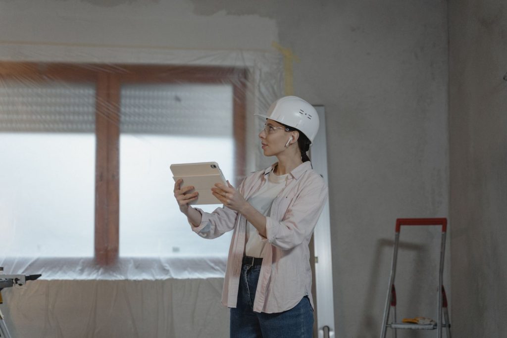 Conductrice de travaux casquée relevant l’avancement d’un chantier de rénovation sur une tablette